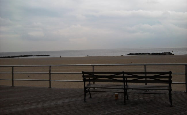 Empty bench looking out at a cloudy beach on Coney Island